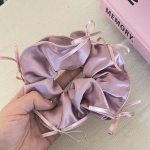 Handheld pale pink satin scrunchie with delicate ribbon bows and ballet aesthetic