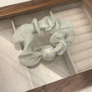 Detail of light green pleated chiffon scrunchie with iridescent pearl on a wooden box