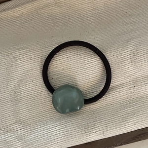 Detail shot of irregular grey resin bead on elastic hair tie over beige fabric