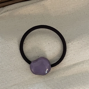 Detailed macro view of an irregular purple resin charm on a black high-elastic hair tie
