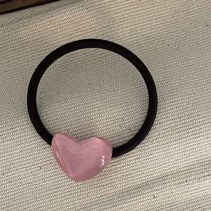 Detail of pink resin heart hair tie with durable black elastic band on beige fabric