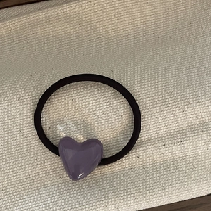 Close-up of purple resin heart charm on high elasticity black hair tie on fabric background