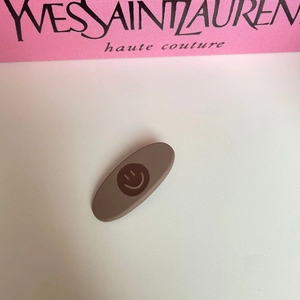 Matte brown oval hair clip with smile face icon on white textured surface background