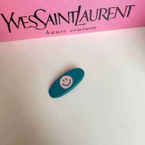 Teal oval hair clip featuring a pink smiley face design on a decorative background