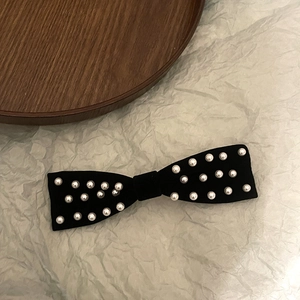 Vintage black velvet bow hair clip with pearls shown at a 45-degree angle on wood