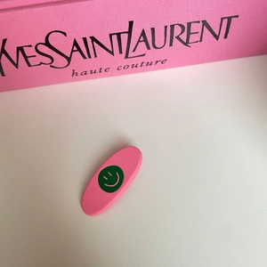 Close-up of pink matte oval hair clip featuring a green smiley face on a soft background
