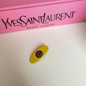 Detail view of yellow matte hair clip featuring a purple smiley face on a white surface