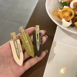 Close-up of matte resin hair clips in nude and olive colors with gold lettering details