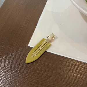 Olive green seamless duckbill hair clip with gold metal base on a white ceramic plate