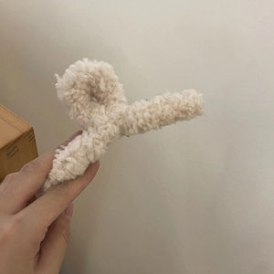Detail of soft cream plush hair claw clip held by hand for winter hair styling accessories