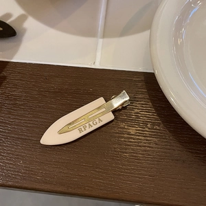 Close-up of a beige seamless hair clip with RPAGA text and gold metal duckbill clip