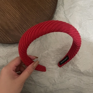 Detail of red knitted headband with handmade label and thick braided texture