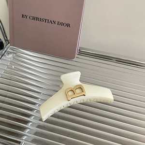 Pince à cheveux crème minimaliste avec lettre B dorée sur un plateau texturé