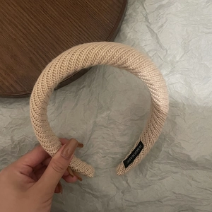 Detail of warm beige thick knitted headband featuring a handmade fabric label on the side