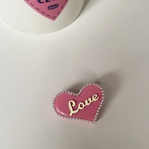 Detail einer dunkelrosa Herz-Haarklammer mit weißen Perlen und Love-Schriftzug