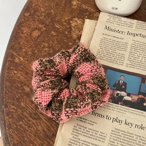 Detailed view of pink and brown checkered knit scrunchie on vintage wood and newspaper