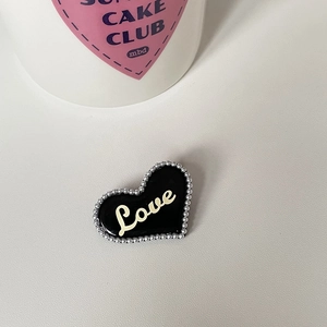 Detail einer schwarzen herzförmigen Haarspange mit Silberperlen und Love-Schriftzug