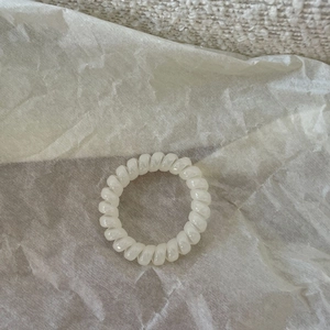 Close-up of pearl white spiral hair tie with a glossy finish on minimalist paper texture