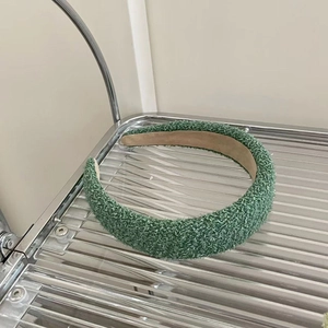 Detail view of green teddy fleece headband with non-slip brown lining on glass rack