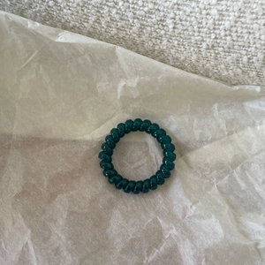 Close-up of a dark green spiral telephone wire hair tie with a glossy jelly finish