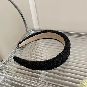 Detail of a thick black fuzzy headband on a tray showing soft texture and brown lining