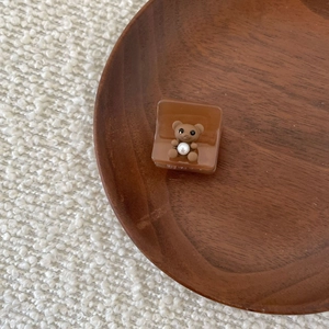Brown acetate hair claw clip with cute 3D bear and pearl detail on wooden tray
