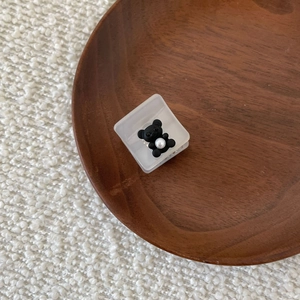 Detail view of a mini white bear hair claw clip with a pearl on a wooden plate