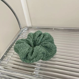 Close-up of grass green scrunchie made of thick plush fabric on a metal shelf