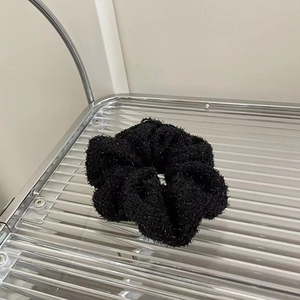 Detail of black plush scrunchie with glitter sparkle and soft knit texture on metal rack