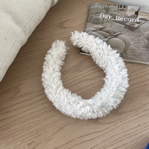 Close-up of a white fluffy faux lamb wool headband placed on a modern wooden background