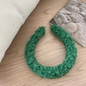 Detailed texture of forest green faux shearling headband on a natural wooden background