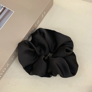 Close-up of elegant black satin scrunchie showing glossy fabric texture and soft pleats