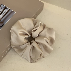 Detail view of champagne satin scrunchie showing smooth glossy silk texture and folds