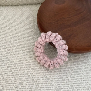 Close-up of pink spiral knitted hair tie on a wooden tray with soft fabric texture