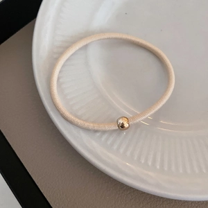 Minimalist beige elastic hair tie with a gold bead decoration on a ceramic plate