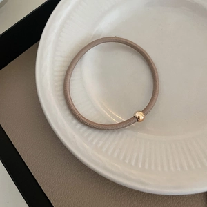 Elastic hair tie in coffee brown with polished gold bead on elegant ceramic plate