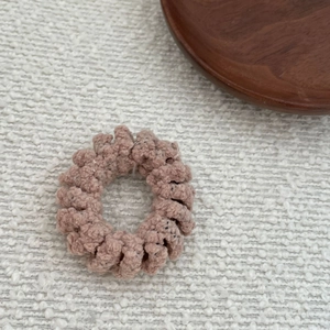 Dusty pink wool spiral telephone cord hair tie on a rustic wooden plate and white fabric