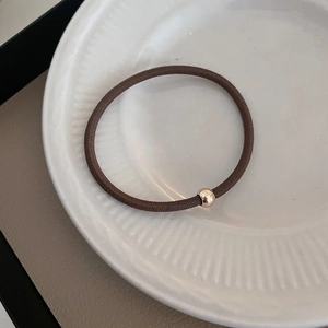 Detail of durable brown elastic hair tie with a polished gold bead on ceramic plate