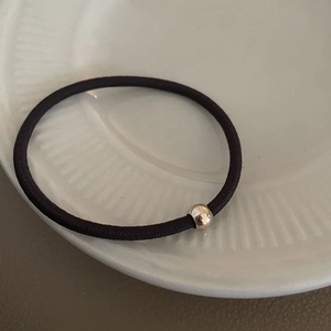 Close-up of a high-elastic black hair tie with a polished gold bead on a ceramic plate