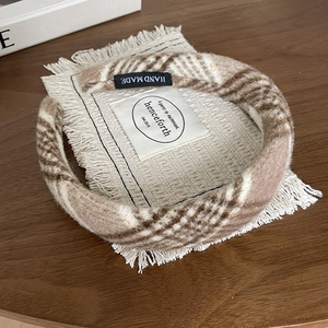 Detail of a brown plaid woolen headband with handmade label on a cozy woven mat