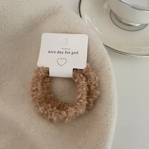 Close-up of two brown teddy fleece hair scrunchies on a soft cream wool hat