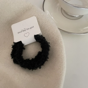 Detailed close-up of a plush black faux fur hair tie on a decorative paper display card