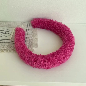 Close-up of fluffy rose pink lamb wool headband with curly fleece texture and wide band