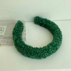 Detail of dark green teddy fleece headband with soft curly wool texture on white surface