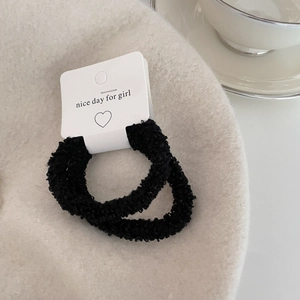 Close-up of two soft black faux fur scrunchies on a minimalist display card
