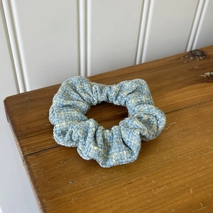 Detail of tweed scrunchie featuring light blue and beige woven pattern on wooden surface