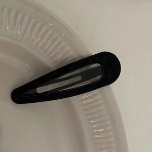 Detail of a black checkered snap hair clip with a classic teardrop shape on a white tray