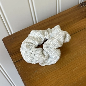 Detail of grey tweed fabric hair scrunchie with textured weave on a wooden table surface