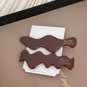 Détail de barrettes à cheveux ondulées en acétate marron foncé avec lettrage doré