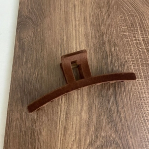 Detail view of large dark brown flocked shark clip on wooden surface with metal spring